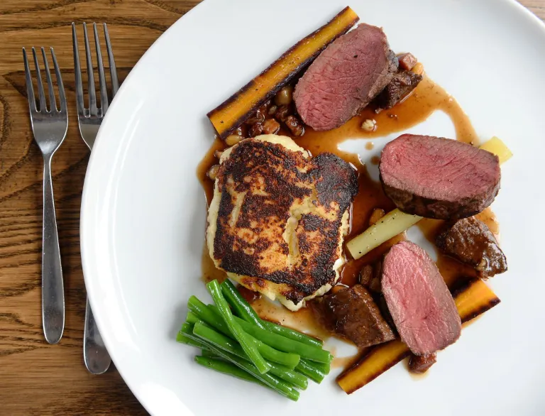 Meat and vegetables including parsnips and green beans on a plate.