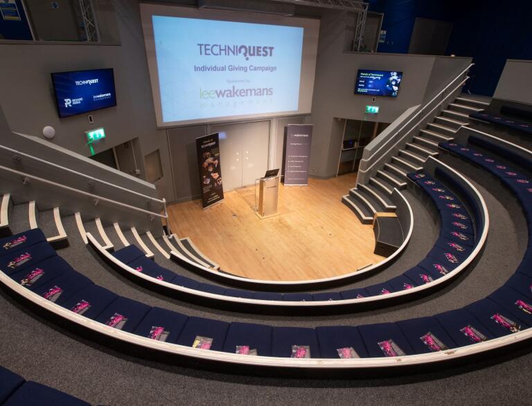 A conference amphitheatre surrounding a screen and speaking podium.