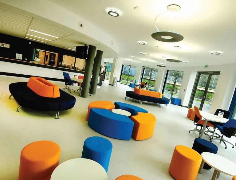 A foyer surrounded by large windows with colourful upholstered seats in a university.