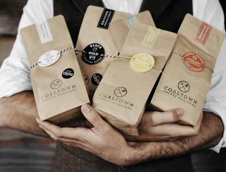 Man holding four paper bags of Coaltown Coffee.