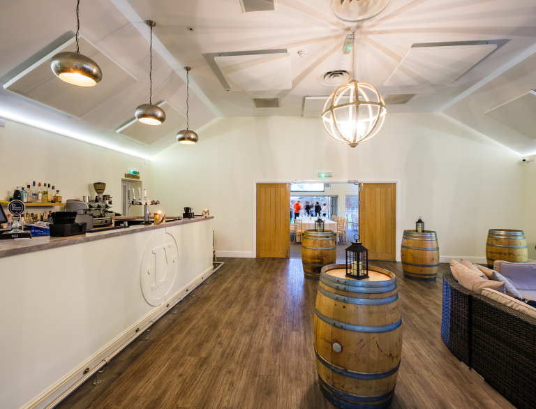 A bar area with barrels as tables and a meeting room which can be seen through a door.