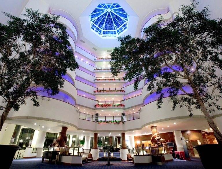 A large atrium in a luxury hotel with symmetrical trees and a glass dome roof.