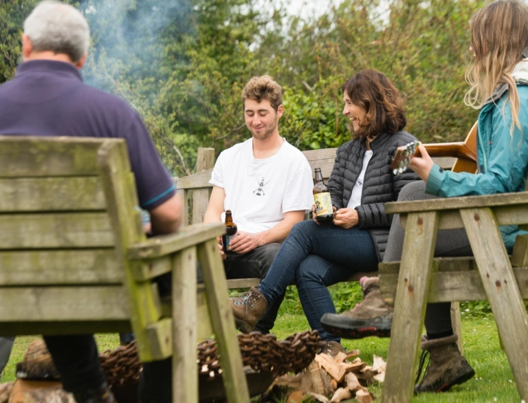 People sat around a camp fire on benches.