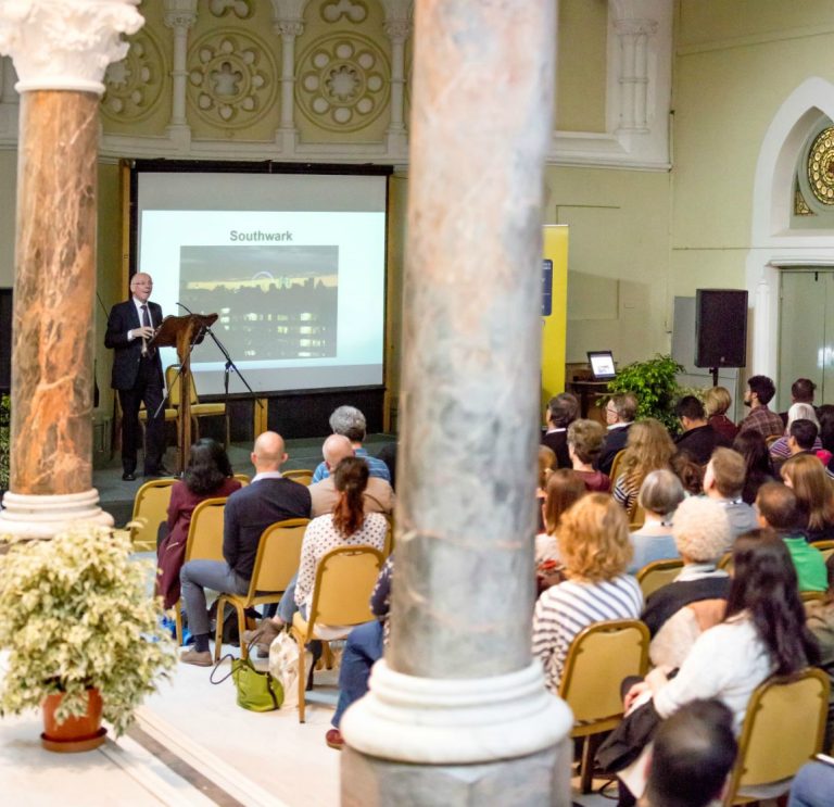 A group of people watching a presenter and screen in a university conference hall.