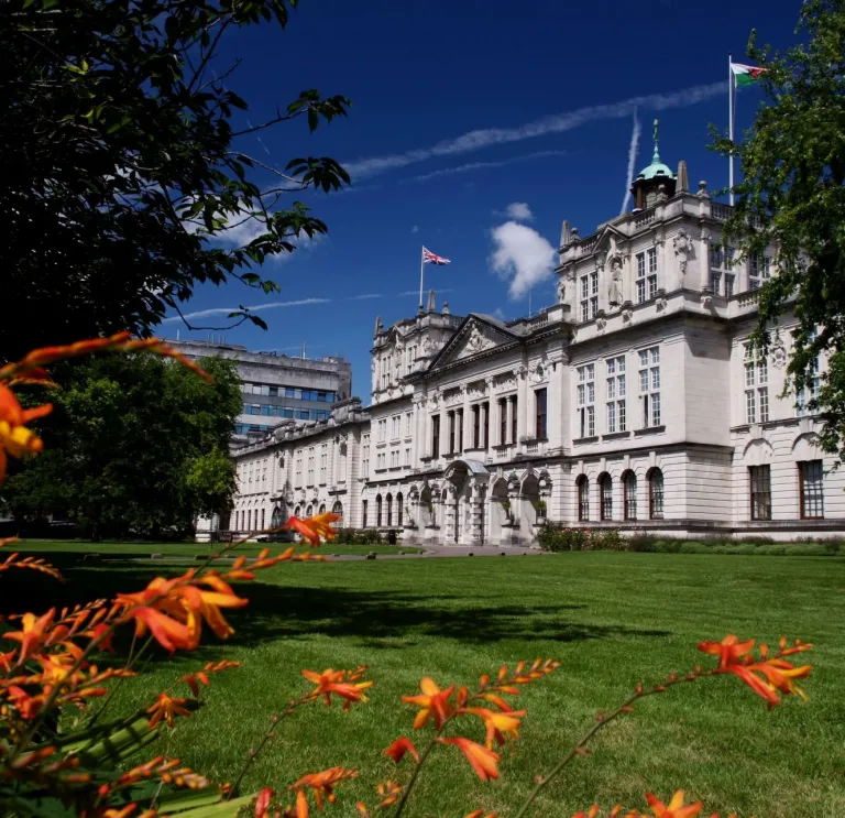 An external view of a university building framed by trees and flowers.
