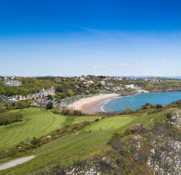 Views of golden sands and the ocean from a golf course up on a cliff.