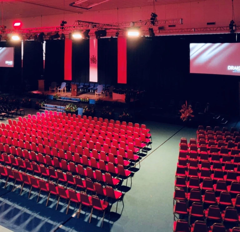 A large theatre style meeting venue, looking out at a stage and display screen.