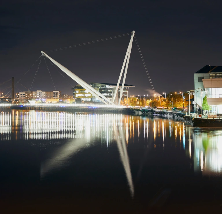Newport city footbridge at night with lights reflecting in the water.