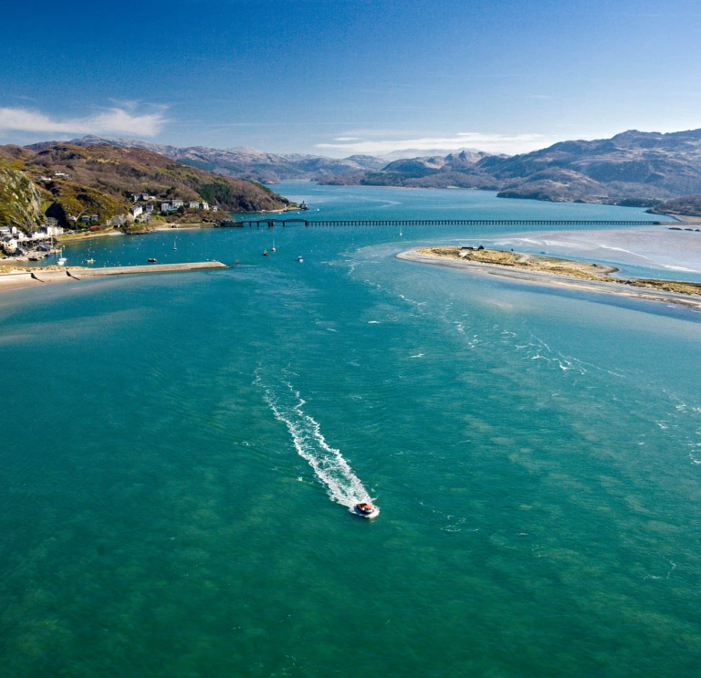 Aerial view of a boat travelling down an estuary between sandy coves.