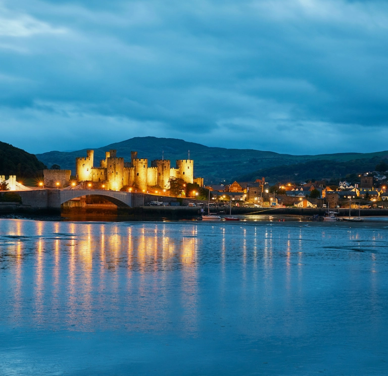Conwy Castle lit up at night and reflecting in the water.