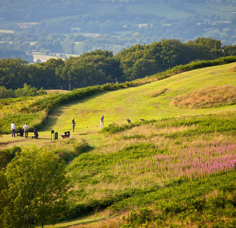 Golfers playing a round with views of the countryside beyond.