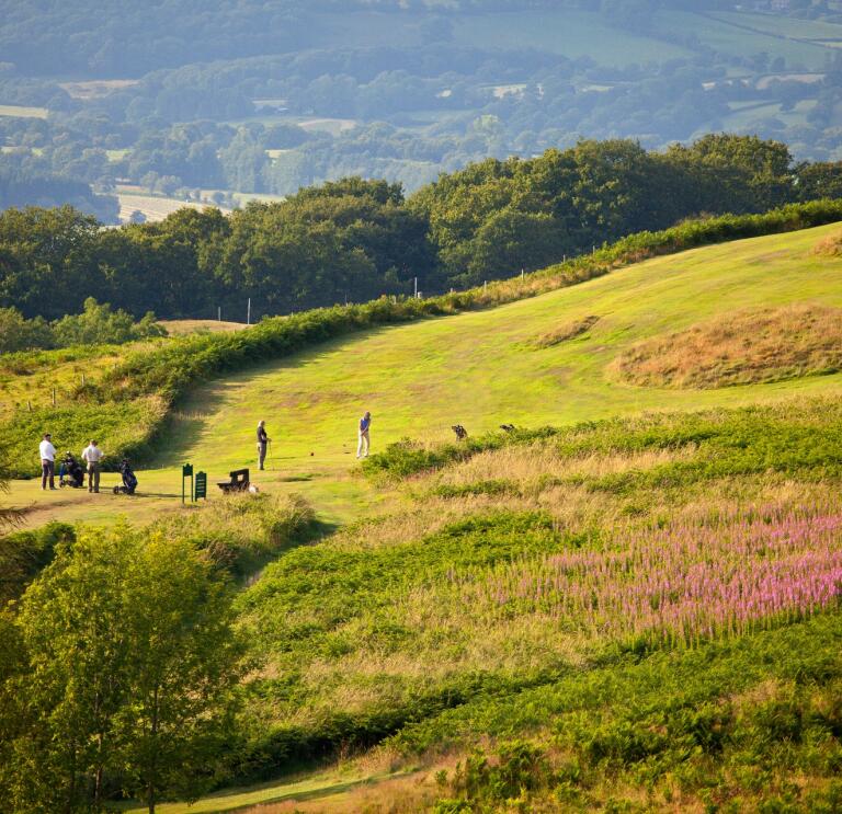 Golfers playing a round with views of the countryside beyond.