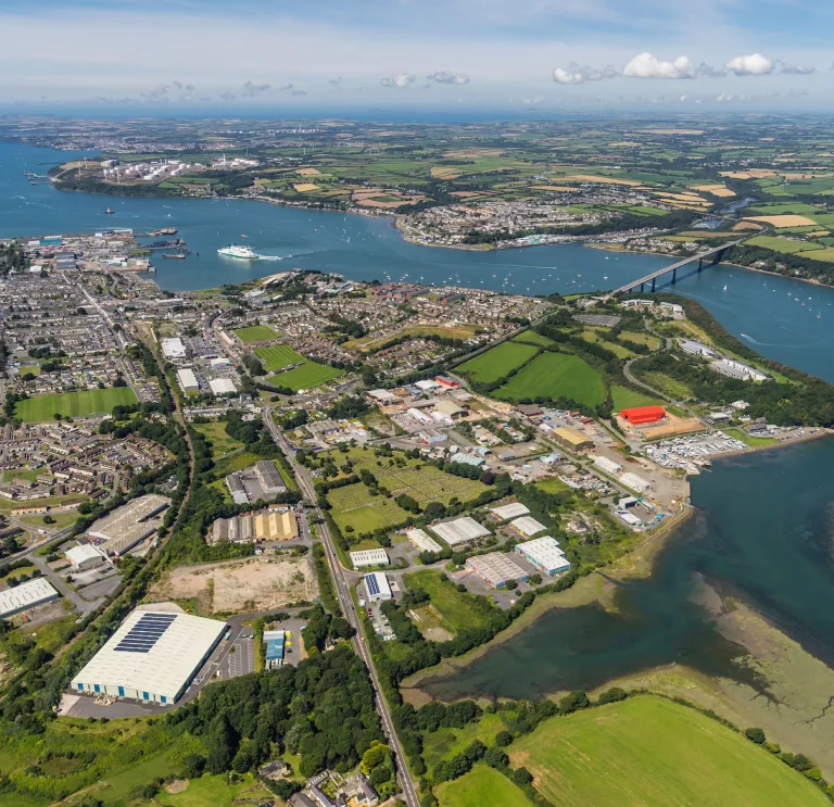 Aerial shot of sea and bridge crossing waterway with lots of businesses set up on green land.