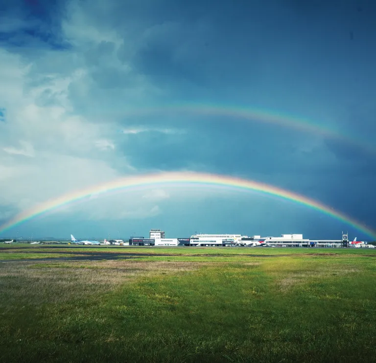 Rainbow over the landing field at airport and white buildings in background.