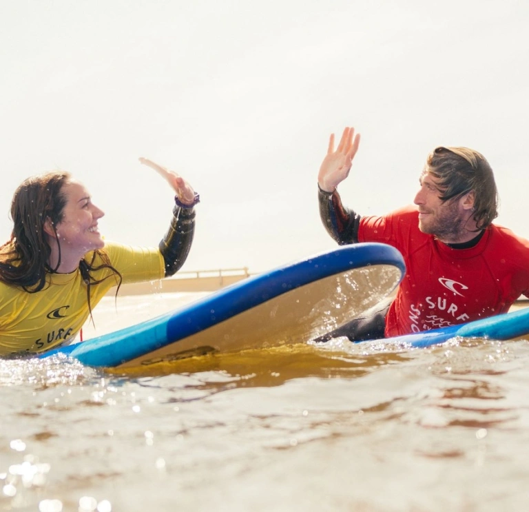2 people on a surfboard doing a high five.