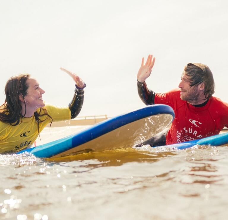 2 people on a surfboard doing a high five.