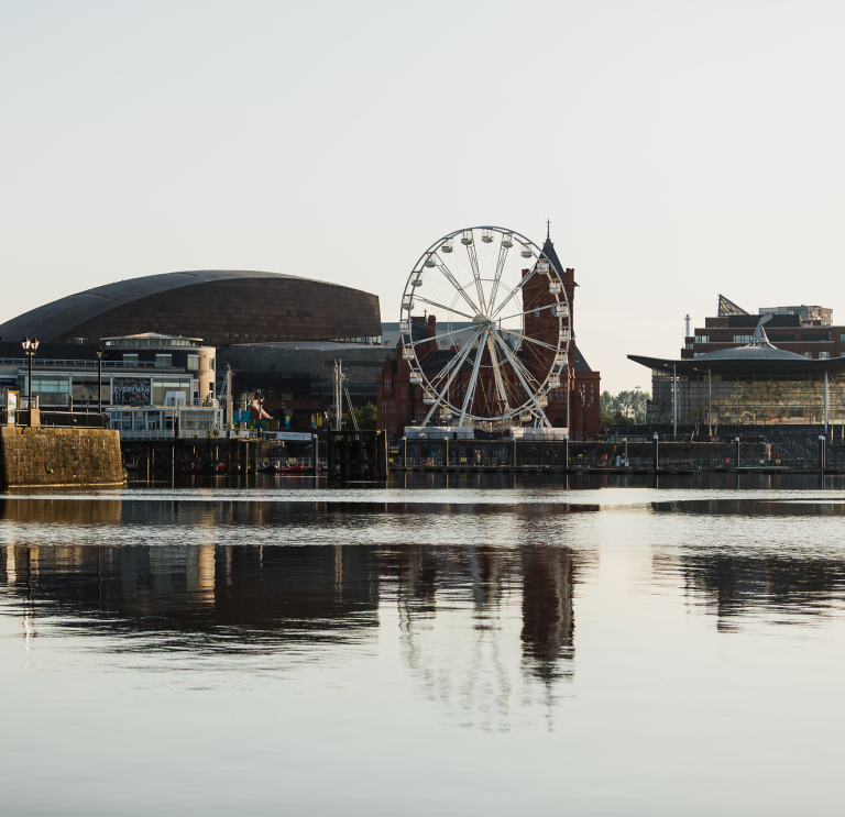 Landscape of Cardiff Bay with buildings and big wheel reflecting in the water.