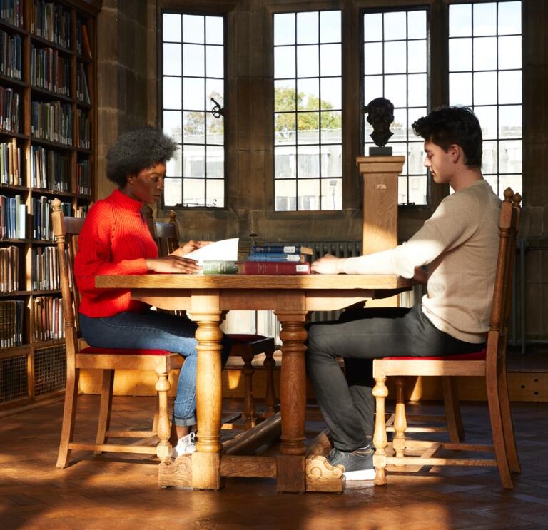 Two students in a university library sitting at a desk 