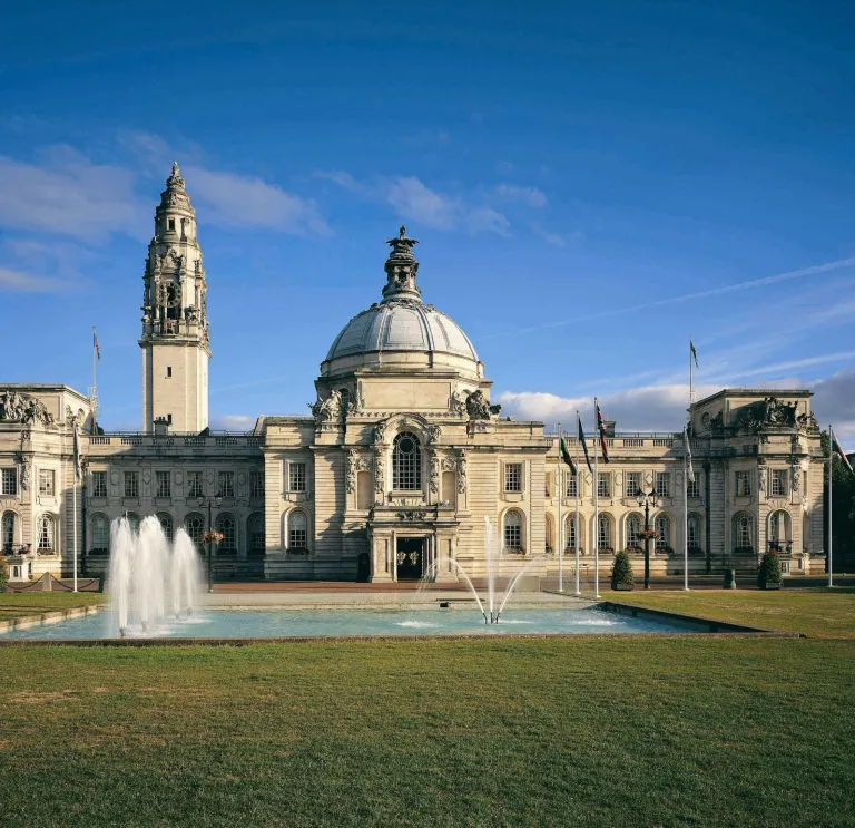 A city hall with a fountain on the lawns at the front of the building.