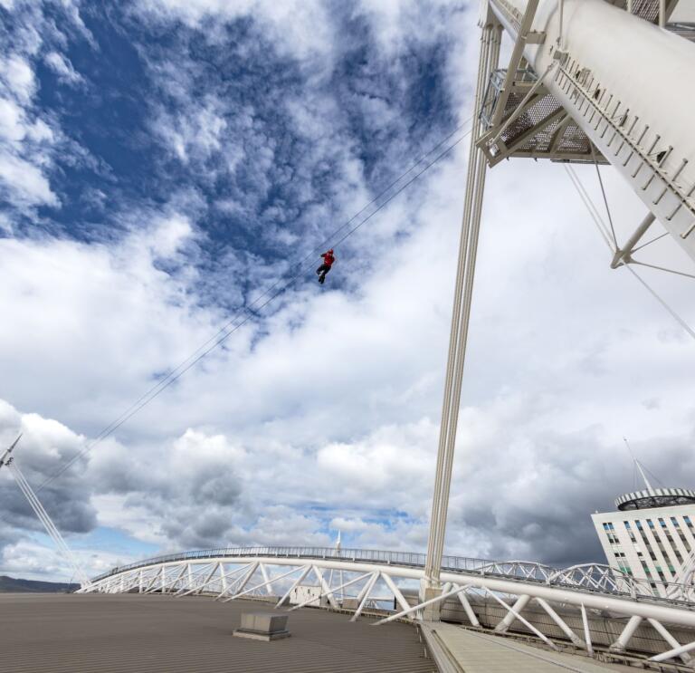 A person ziplining above the roof of a sports stadium.