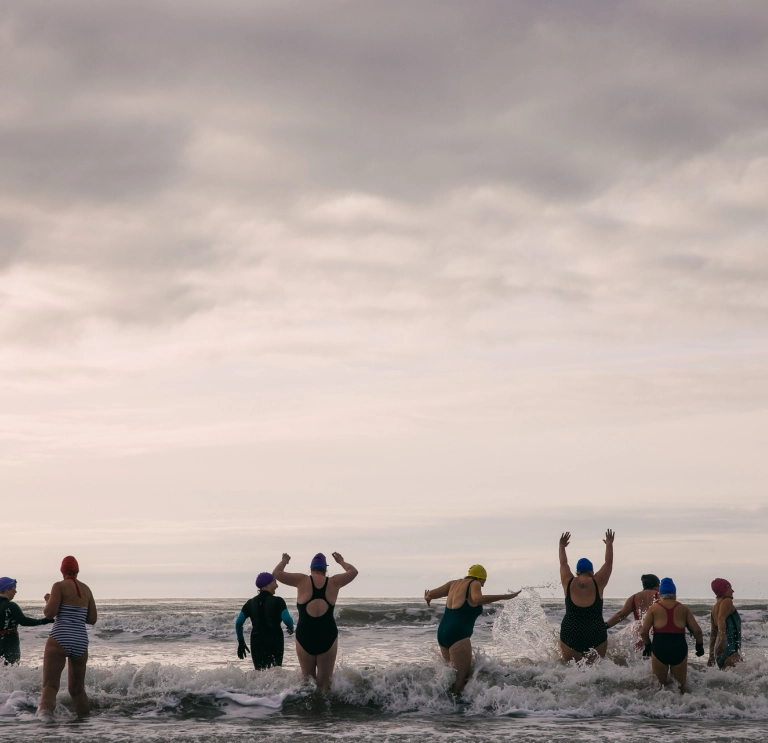 women in bathers running  into the sea cheering and laughing 