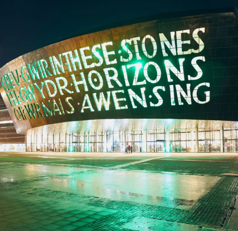 outsideof the wales millennium centre at night with words written into the building lit up 