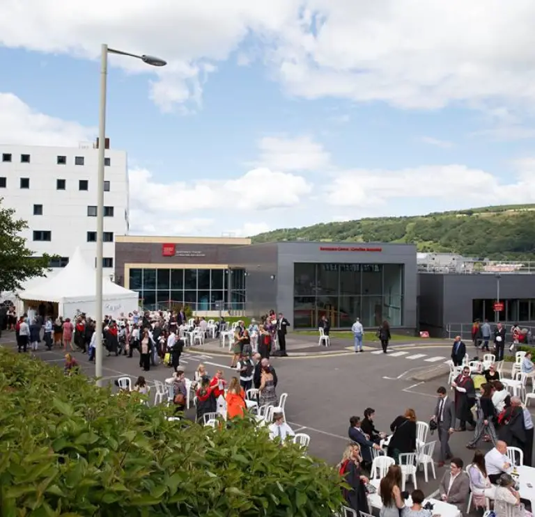 image of foyer exterior of the Trefirest campus with peopole on plastic seats and standing talking 
