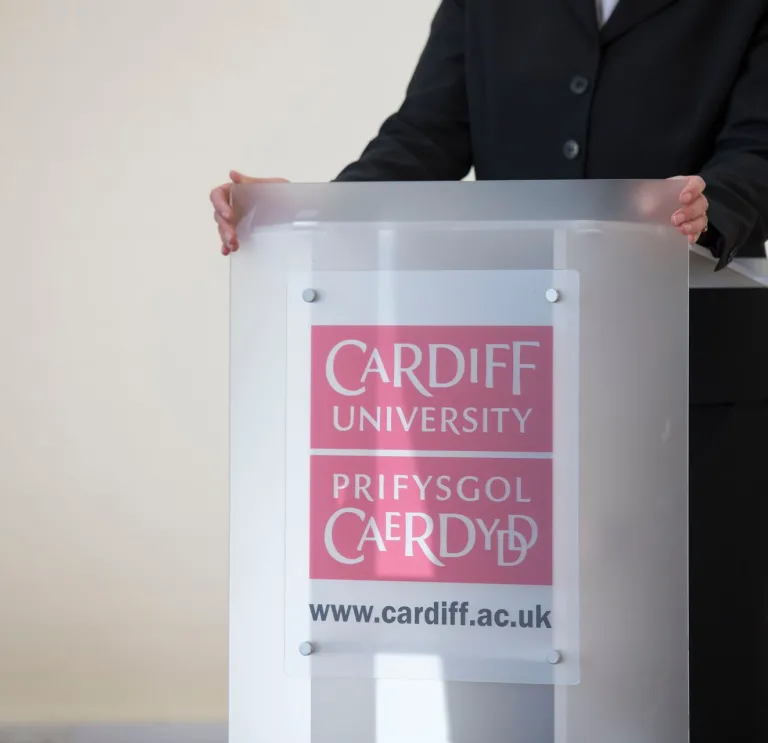 lecturers hands resting on podium wuth Cardiff University bilingual branding 