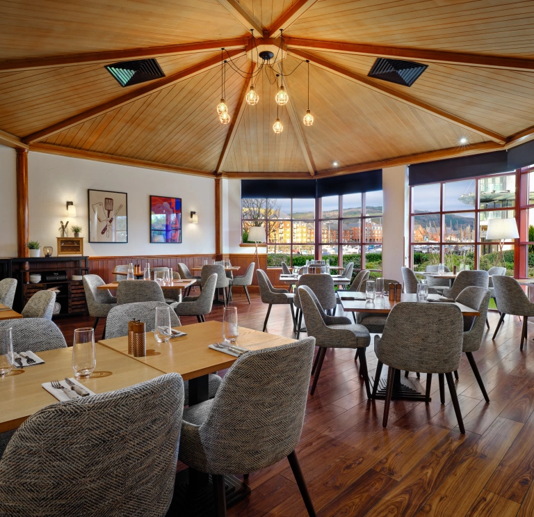 Bright, modern restaurant with wooden floors, large windows, and neatly arranged dining tables.