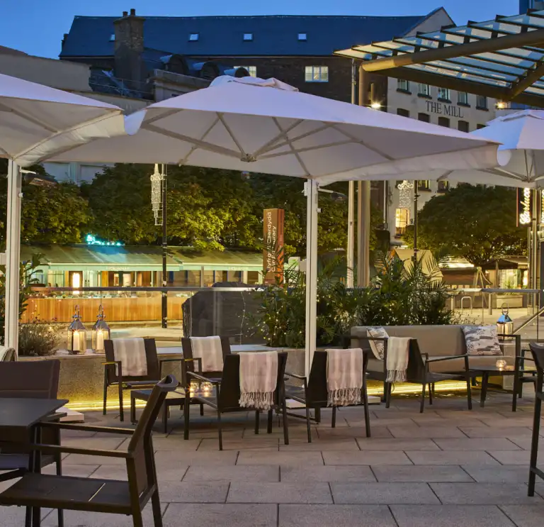 Outdoor terrace with seating, large white parasols and warm ambient lighting
