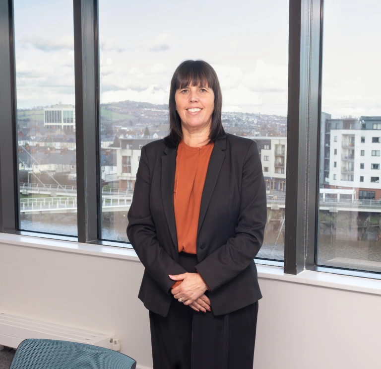 Person standing in front of large windows overlooking a city waterfront.