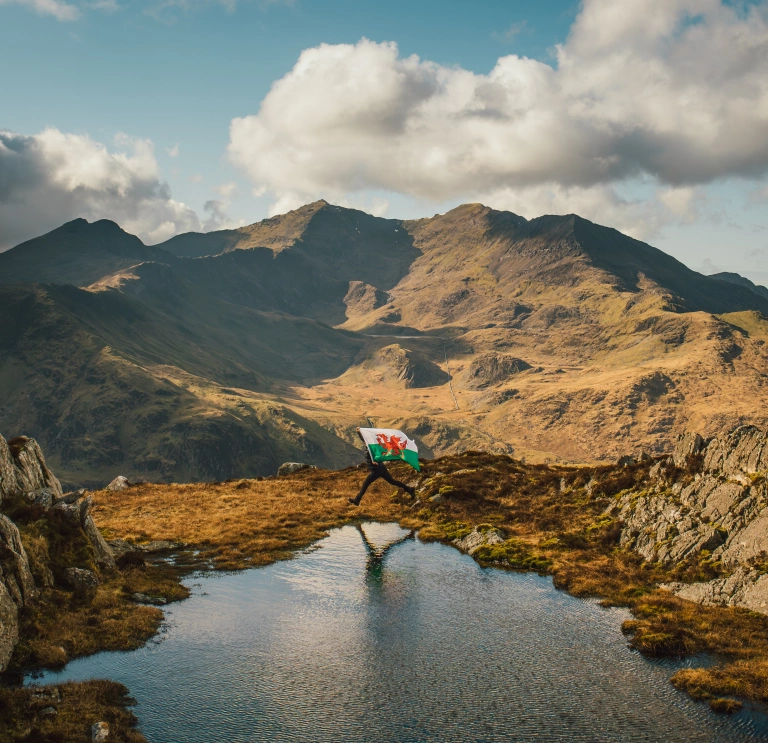 Person holding a Welsh flag overlooking Snowdonia mountain landscape