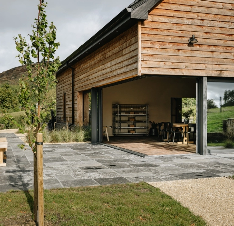 Modern timber-clad venue with open-plan interior and outdoor terrace in a rural landscape setting.