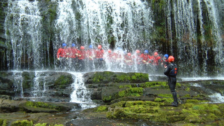 Group in safety gear standing behind a waterfall.