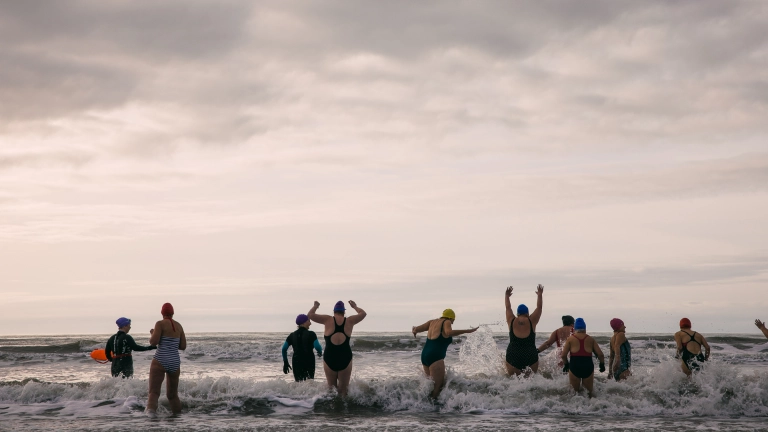 women in bathers running  into the sea cheering and laughing 