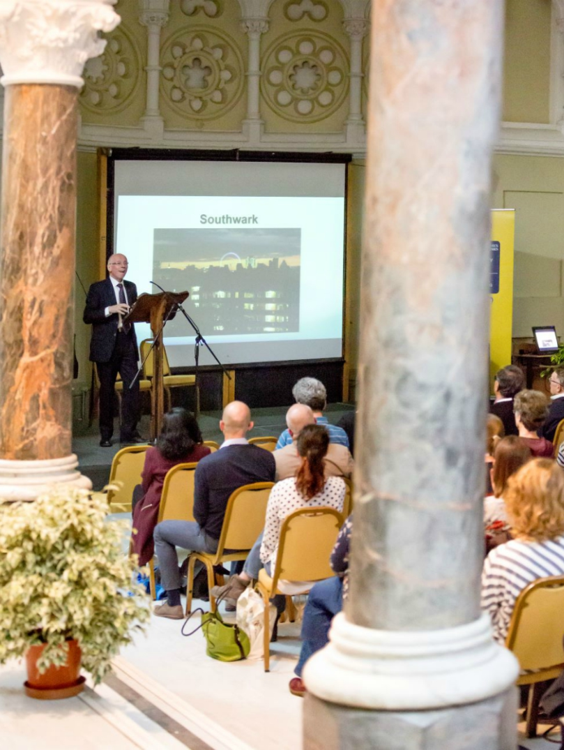 A group of people watching a presenter and screen in a university conference hall.