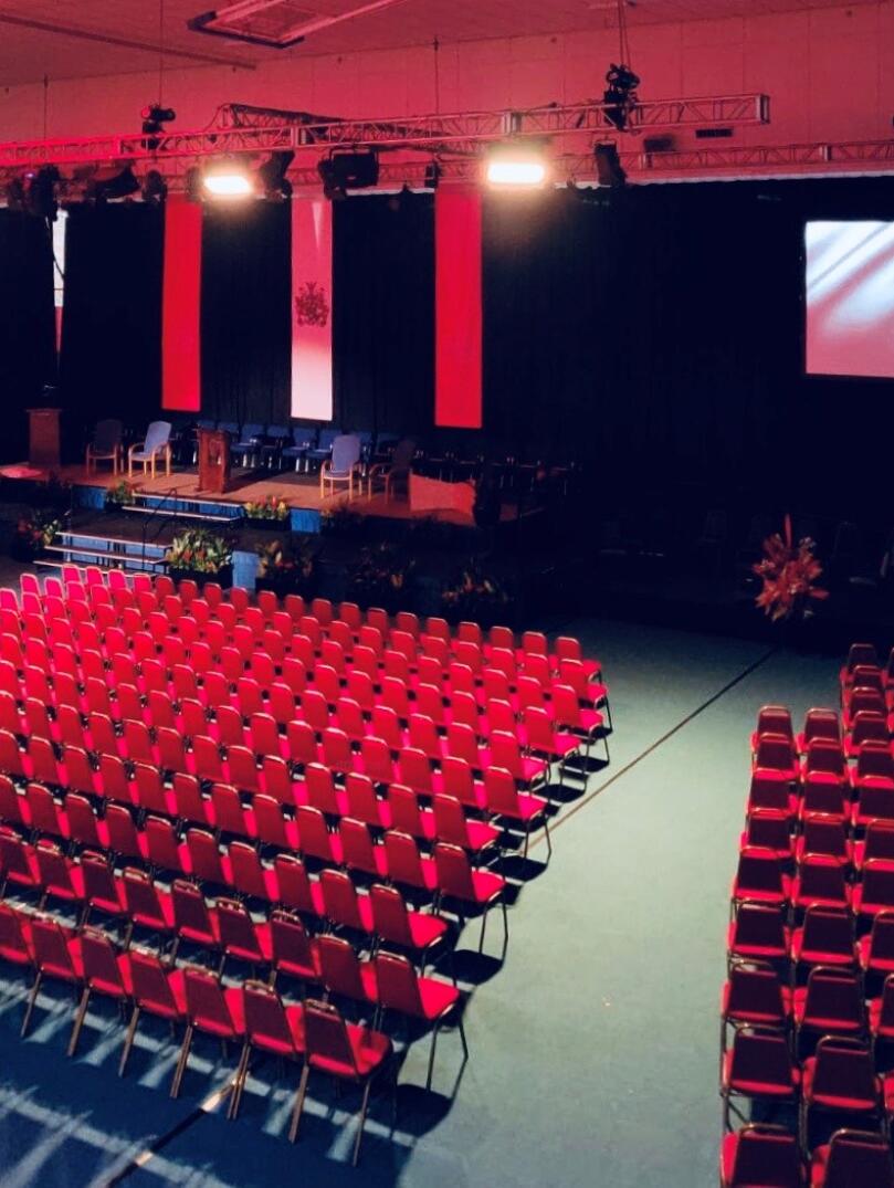 A large theatre style meeting venue, looking out at a stage and display screen.
