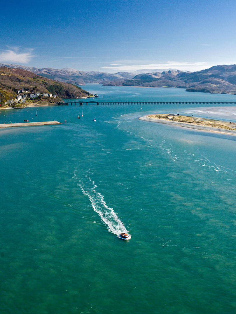 Aerial view of a boat travelling down an estuary between sandy coves.