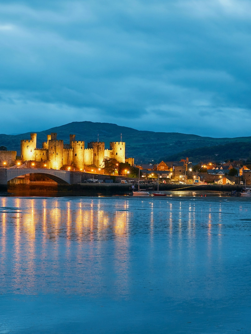 Conwy Castle lit up at night and reflecting in the water.