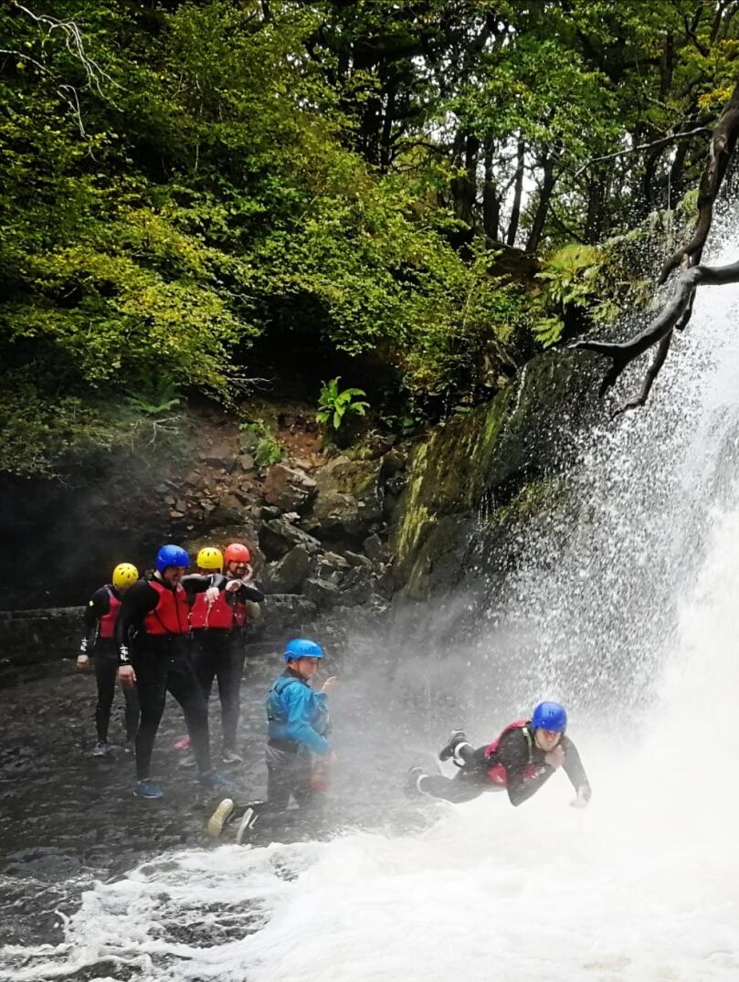 Group of adults with instructors jumping into a waterfall.
