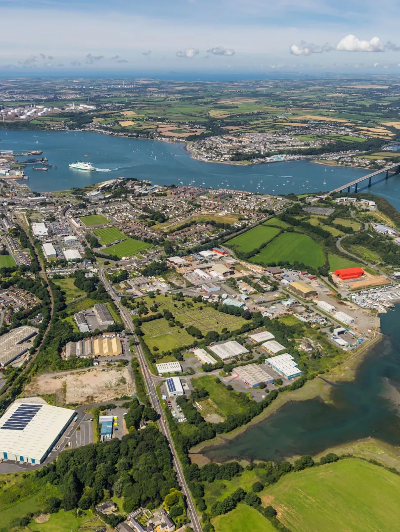 Aerial shot of sea and bridge crossing waterway with lots of businesses set up on green land.