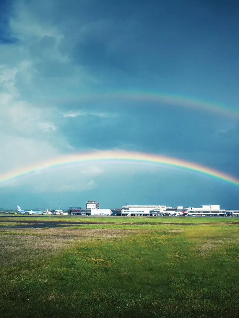 Rainbow over the landing field at airport and white buildings in background.