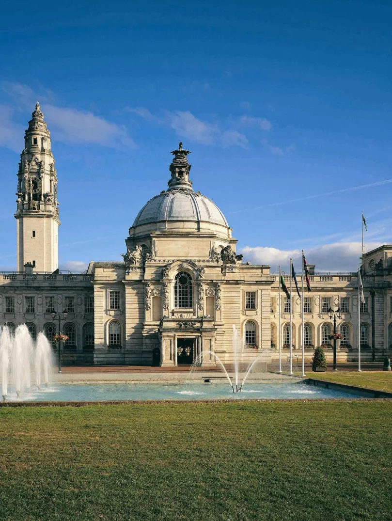 A city hall with a fountain on the lawns at the front of the building.