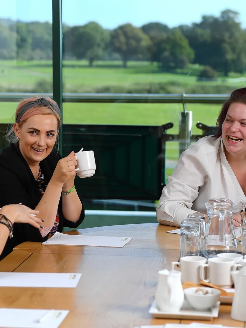 people laughing while in a meeting around the table with the racecourse in the background 