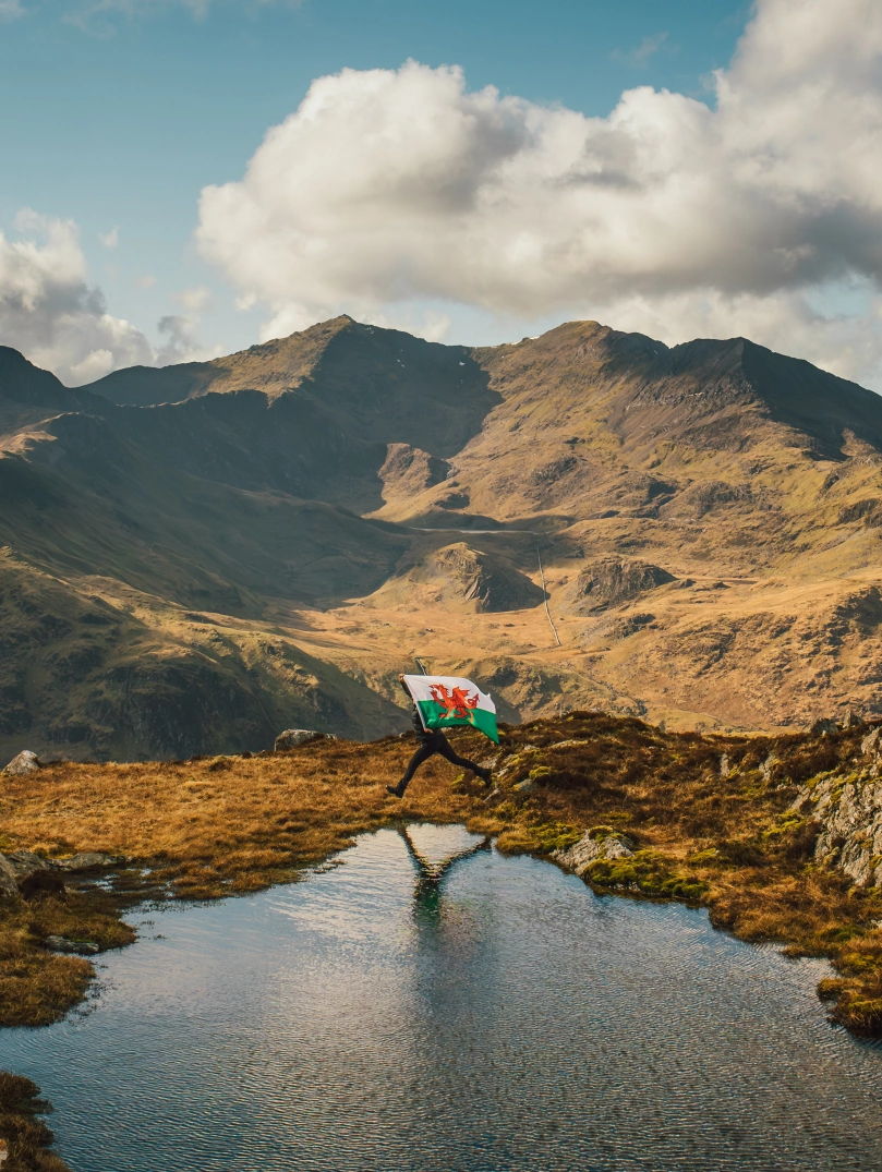 Person holding a Welsh flag overlooking Snowdonia mountain landscape