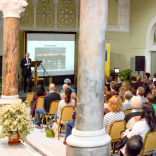 A group of people watching a presenter and screen in a university conference hall.