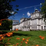 An external view of a university building framed by trees and flowers.