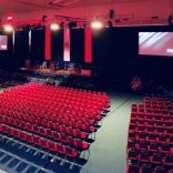 A large theatre style meeting venue, looking out at a stage and display screen.