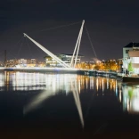 Newport city footbridge at night with lights reflecting in the water.