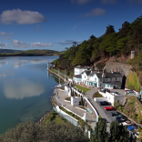 An aerial view of a hotel on the edge of an estuary with mountains beyond.